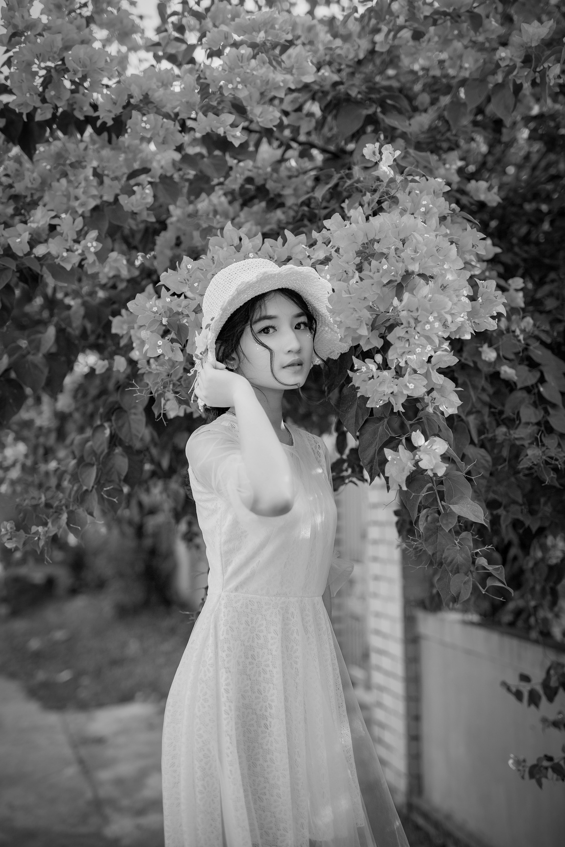 Woman Holding Her Hat While Standing In Front Of Pink Bougainvillea Flowers