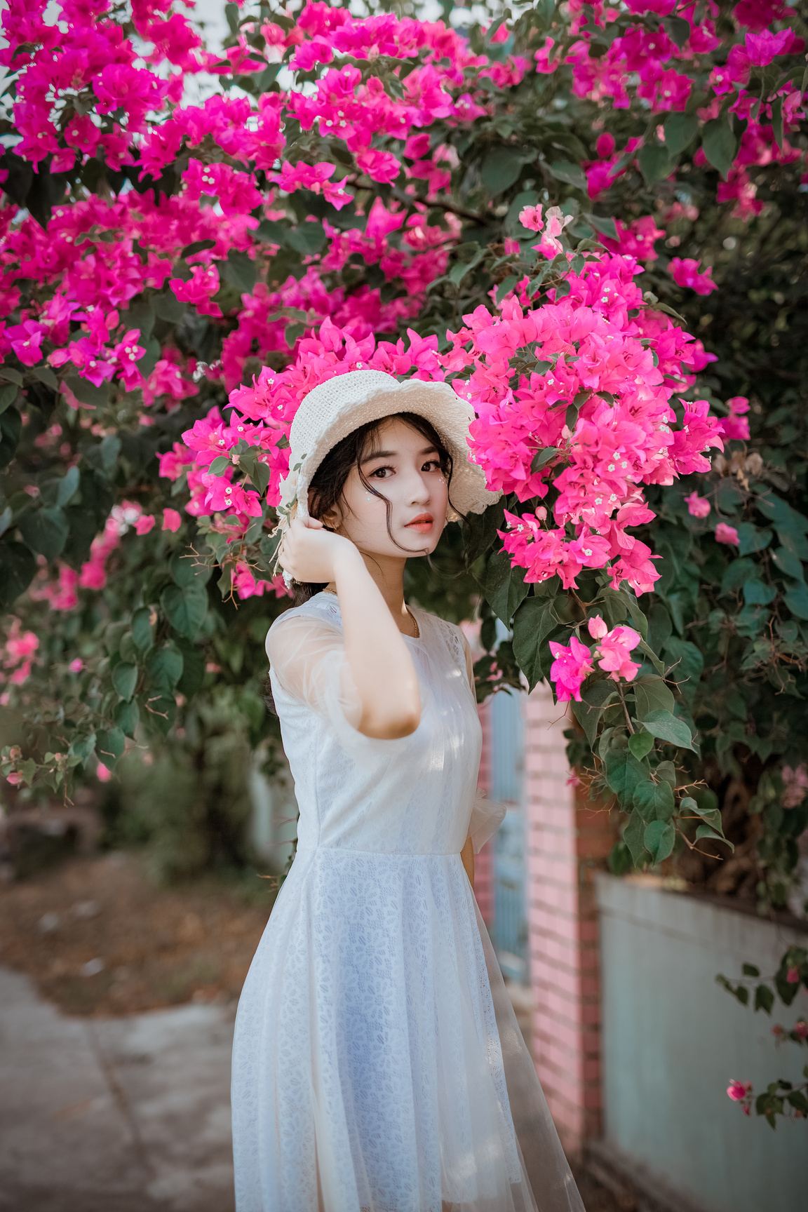 Woman Holding Her Hat While Standing In Front Of Pink Bougainvillea Flowers